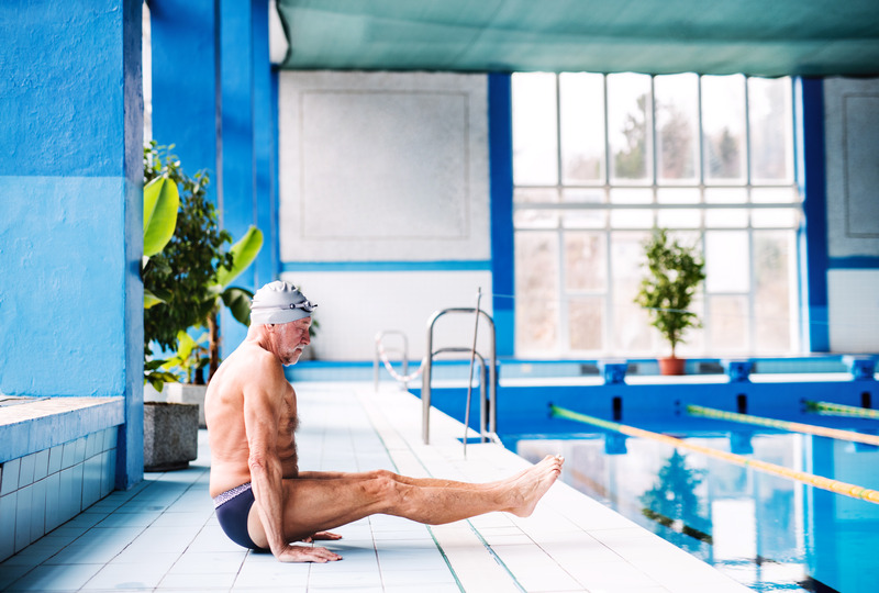 Senior man stretching by the indoor swimming pool.
